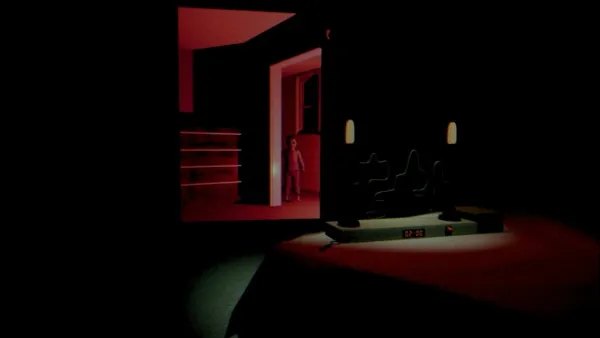 A dimly lit room with a red tint, featuring a small table with two chairs and a lamp. A person stands in the doorway of an adjacent room, which is also illuminated by red lights. The overall atmosphere is mysterious and slightly eerie.